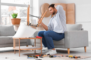 Thoughtful young man assembling chair at home