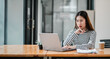 © Satori Studio - A woman is sitting at a desk with a laptop in front of her. She is looking at the screen with a serious expression on her face