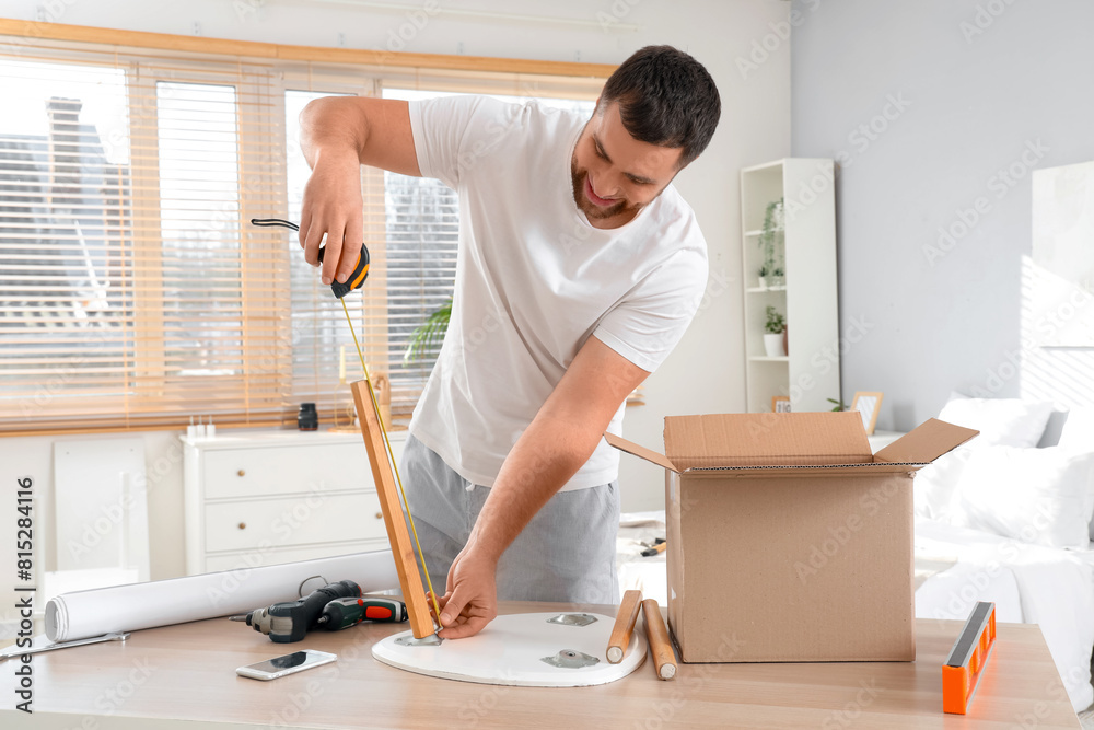 Young man with tape measure assembling table in bedroom