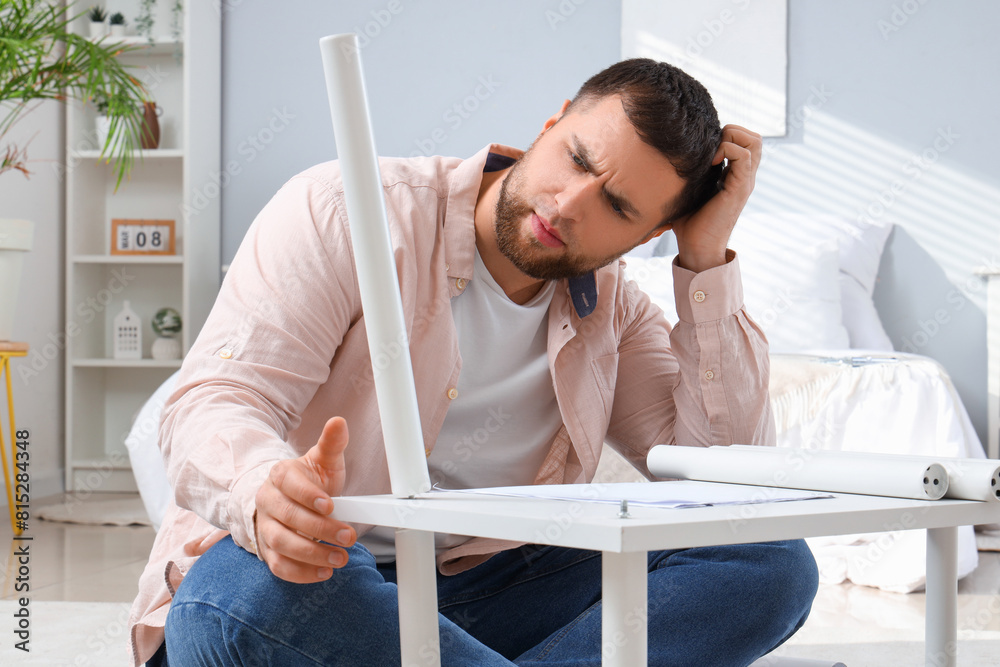 Thoughtful young man assembling shelf unit in bedroom