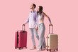 © Pixel-Shot - Beautiful young happy couple of tourists with suitcases and headphones on pink background