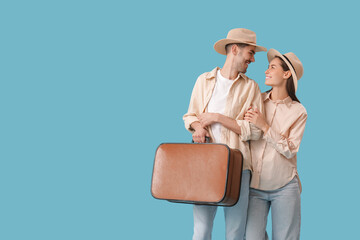 Wall Mural - Beautiful young happy couple of tourists with suitcase on blue background