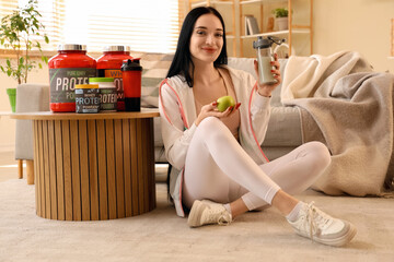 Canvas Print - Sporty young woman with protein shake and apple sitting at home