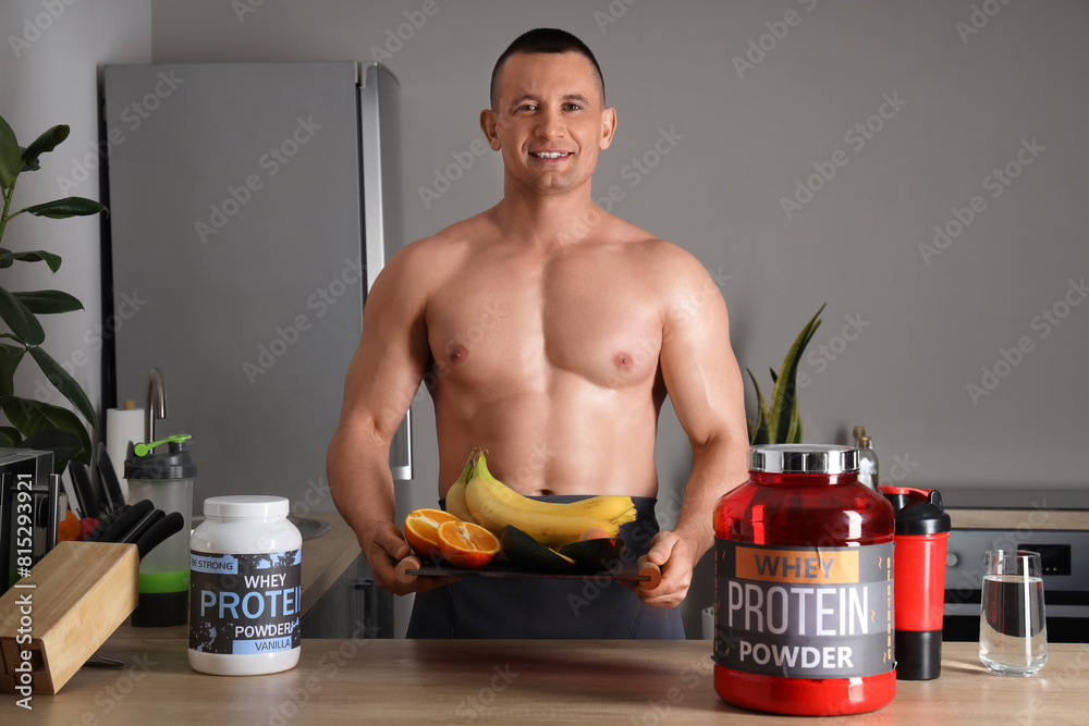 Handsome muscular man with food and protein powder on table in kitchen