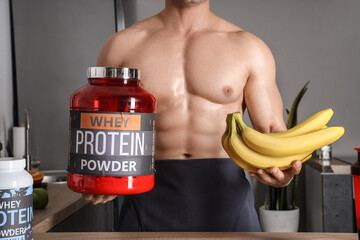 Canvas Print - Handsome muscular man with protein powder and bananas in kitchen, closeup