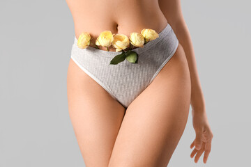 Wall Mural - Beautiful young woman in panties with rose flowers on grey background, closeup