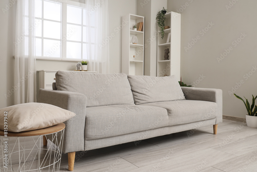 Interior of light living room with grey sofa and shelf units