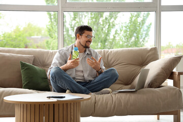 Canvas Print - Young man with bottle of cucumber water video chatting on sofa at home