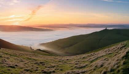 Wall Mural - A grassy hilltop with a panoramic view of the surrounding countryside during sunrise. 