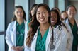 © trustmastertx - A group of young female doctors in white coats stand together, the backdrop is an office with medical equipment visible on the shelves behind them. They come from different ethnicities