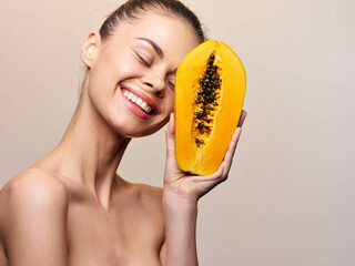 Beautiful young woman with papaya fruit facial mask, skincare and beauty concept, isolated on beige background