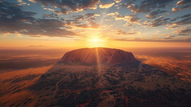 Aerial view of Uluru (Ayers Rock) in Australia, with its massive red sandstone formation rising from the flat desert landscape at sunset.     