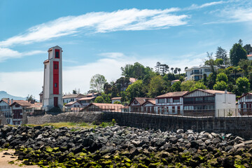 Em meio a um céu azul e parte de cidade de Saint Jean de Luz, um farol à beira mar para orientação da navegação marítima