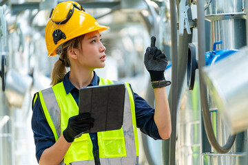 Professional Asian woman engineer in safety uniform working on digital tablet at outdoor construction site rooftop. Industrial technician worker maintenance checking building exterior air HVAC systems