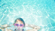 Child with goggles making a playful face underwater in a clear p