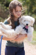 Girl holding a playful white puppy outdoors on a sunny day