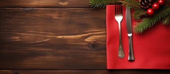 Poster - Top view of a red napkin with a wooden background showcasing a spoon knife and fork alongside a fir tree branch Ample copy space available for showcasing your content such as a menu or advertising