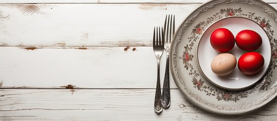Poster - A top down view of a plate with vintage silverware and red Easter eggs on a white shabby wooden table creating a visually appealing copy space image