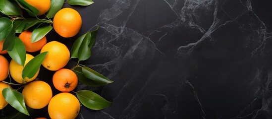 Poster - Top view of a flat lay fruit composition featuring an orange or tangerine with leaves placed on a black stone background The image provides copy space for text or other elements