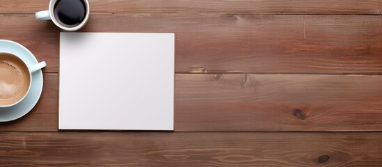 There is a top down view of a wooden work table with a notepad a computer and a coffee cup placed on it creating enough space for additional content in the image