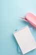 A vertical minimalist back to school setting with a stack of pastel notebooks and a pink pencil case containing colored pencils, all laid out on a soft blue background