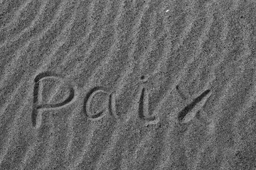Wall Mural - The word PEACE in French. The beautiful word peace is written on the sandy coast. Conceptual inscription on shiny sand and a beautiful seascape background. A word drawn on the beach. Black and white.