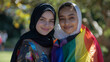 Two happy friends, one with hijab, embracing diversity with rainbow flag