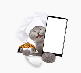 Poster - Happy cat wearing chef's hat looks through a hole in white paper, holds bowl of dry pets food and shows smartphone with white blank screen in it paw, Empty free space for mock up, banner