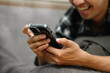 © Prathankarnpap - Cheerful young adult man using mobile phone while lying down on sofa at home