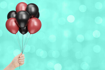 Aufkleber - Female hand holds bunch of red and black balloons on blurred green or aquamarine background. Empty space for text