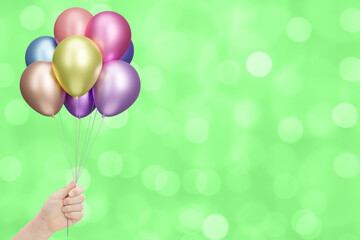 Aufkleber - Childrens hand holds bunch of colorful shiny balloons on blurred summer green background. Empty space for text
