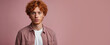 © ginettigino - Portrait of a handsome 25 year old red curly haired guy with a thoughtful, serious and dreamy look wearing a peach colored shirt and is isolated on a light pink background with space for text.