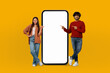 © Prostock-studio - Multiethnic young lovers are standing next to a large phone, appearing to be engaged in conversation or possibly using the phone. The setting is nondescript but suggests a public space.