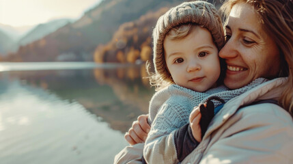 Wall Mural - Smiling mother holding adorable toddler child outdoors,  beautiful nature landscape with lake in the background