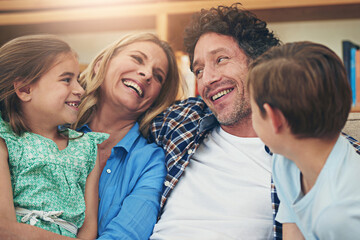 Canvas Print - Laughing, parents and children on sofa for love, playing and bonding together in living room. Lens flare, mother and father with kids on couch for embrace, happiness or weekend break in home