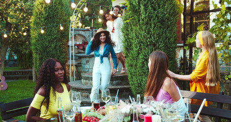 Many diverse happy mixed-races young people entering the garden. Caucasian males and females friends having party outdoors. Asian beautiful girl smiling and greeting a friend. Friendship concept