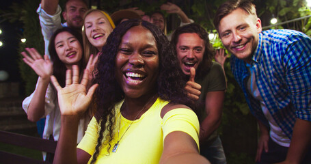 POV of cheerful African American girl talking in good mood. Beautiful Asian and Caucasian girls waving their hands. Handsome happy males smiling. Mixed-races youth at garden party. Talk concept