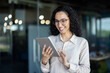 © Liubomir - Smiling businesswoman using a digital tablet in a contemporary office setting, engaging in work activities.