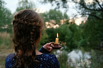 Sticker - Girl with burning candle in candlestick outdoor, abstract natural background. rear view. religion, memory concept. magic, spiritual esoteric ritual. mystery, witchcraft, occultism, wicca, fairytale