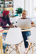 © BullRun - Dark skinned colleagues sitting at desktop in living room using laptop computer for making booking online, african american students talking to each other while cooperate on homework together