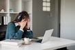 © Natee Meepian - Young woman feeling stressed while wearing headphones and using a laptop in a home office