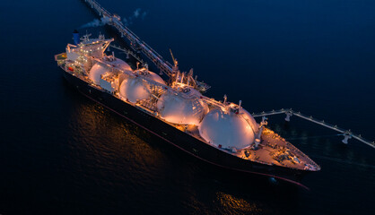 Aerial of Liquified Natural Gas LNG carrier moored to a small gas terminal at night. Fuel crisis. Sanctions.