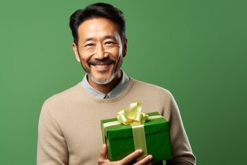 Sticker - Portrait of a satisfied asian man in his 40s holding a gift on soft green background