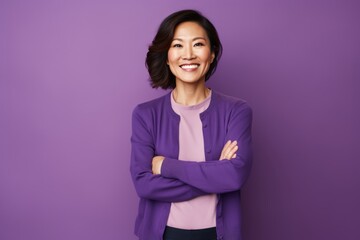 Wall Mural - Portrait of a happy asian woman in her 40s with arms crossed isolated in soft purple background