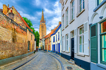 Brugge city historic center, narrow cobblestone street, colorful buildings with brick walls, Bruges old town district, Roman Catholic Parish Church of Our Lady tower, West Flanders province, Belgium