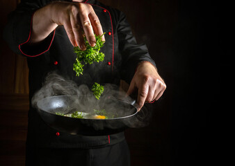 Wall Mural - Cooking scrambled eggs with parsley in a frying pan. The cook hand throws fresh parsley into the scrambled eggs.