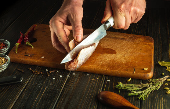 The chef cleans fresh fish with a knife before cooking on the kitchen board.