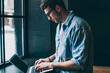 © BullRun - Caucasian male freelancer sitting near cafeteria window and typing new article in modern laptop application, young man blogger browsing wireless internet and updating profile in social networks