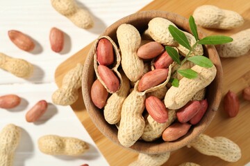 Wall Mural - Fresh unpeeled peanuts in bowl and twig on white table, top view