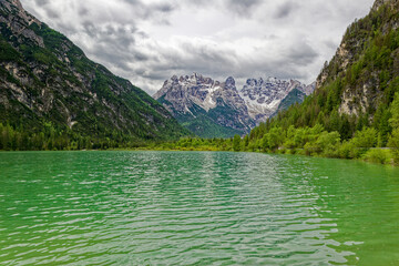 Wall Mural - Green lake in the heart of the Dolomite Mountains. Moody landscape with turquoise water alpine lake Lago di Dobbiaco in Dolomites mountains, Cortina dAmpezzo, Italy on cloudy spring day. Lake Toblache